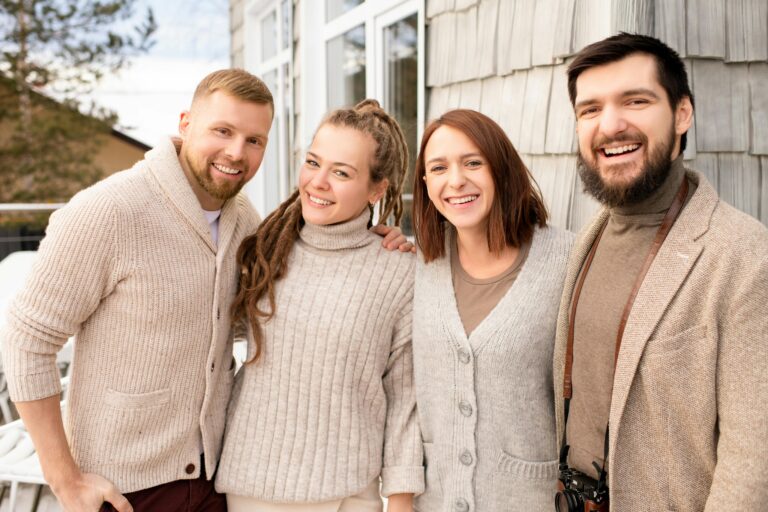 Four happy friends in cozy sweaters share a joyful moment outdoors.